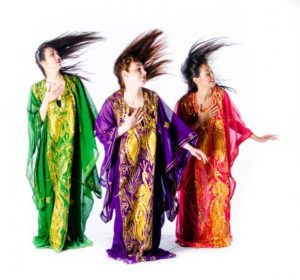 Drie folklore buikdans danseressen in kleurige jurken zwiepen met hun haar 